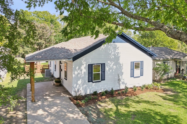 view of front of house featuring a shingled roof, a front lawn, and central AC