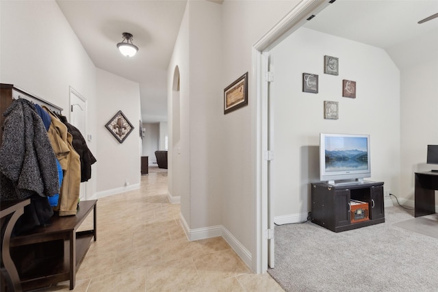 interior space featuring arched walkways, lofted ceiling, light colored carpet, and baseboards