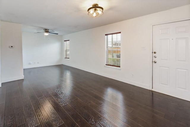 unfurnished living room with dark wood-type flooring, baseboards, and a ceiling fan