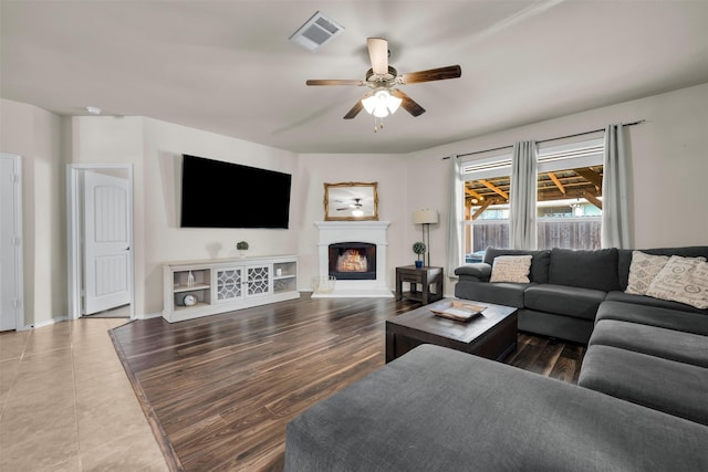 living room featuring a ceiling fan, a warm lit fireplace, visible vents, and wood finished floors