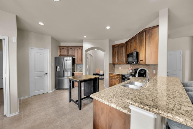 kitchen featuring arched walkways, light stone counters, a sink, backsplash, and black appliances