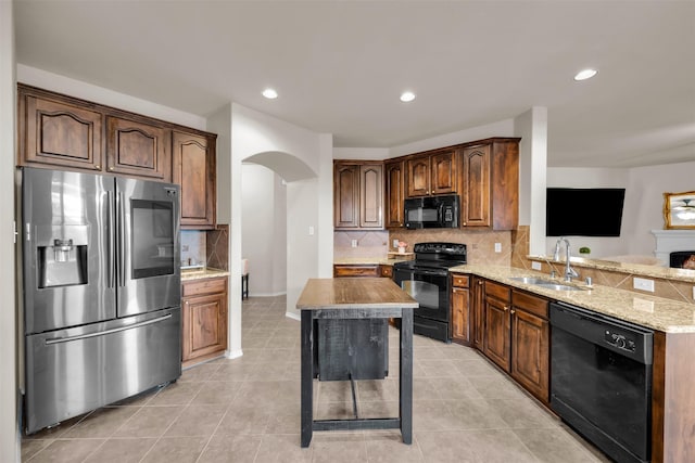 kitchen featuring arched walkways, light tile patterned flooring, a sink, backsplash, and black appliances