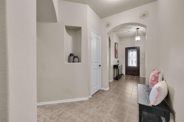 entryway with arched walkways, light tile patterned floors, and baseboards