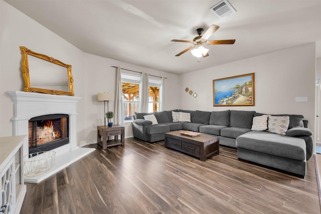 living room with visible vents, ceiling fan, wood finished floors, a warm lit fireplace, and baseboards