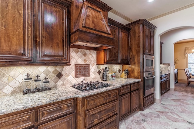 kitchen with light stone countertops, custom range hood, arched walkways, and stainless steel appliances