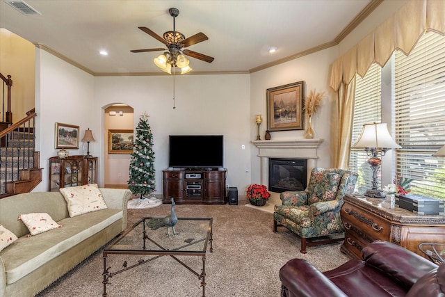 carpeted living area featuring arched walkways, visible vents, stairs, ornamental molding, and a glass covered fireplace