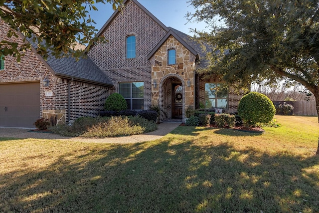 tudor house with a garage, brick siding, a shingled roof, stone siding, and a front yard