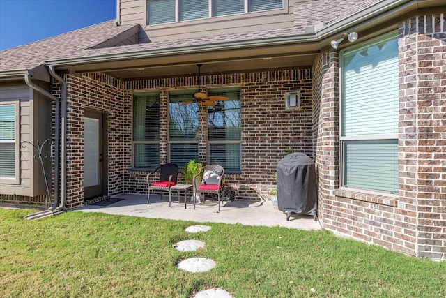 exterior space with roof with shingles, brick siding, a patio, a lawn, and a ceiling fan