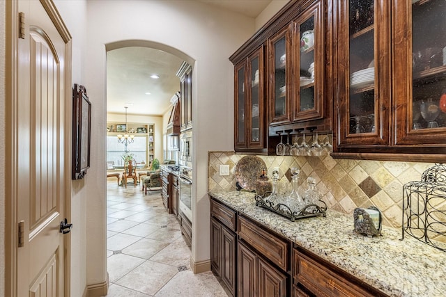 bar featuring light tile patterned floors, arched walkways, a chandelier, stainless steel oven, and backsplash