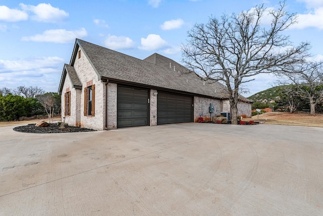 view of side of home featuring a garage, central AC, brick siding, driveway, and roof with shingles