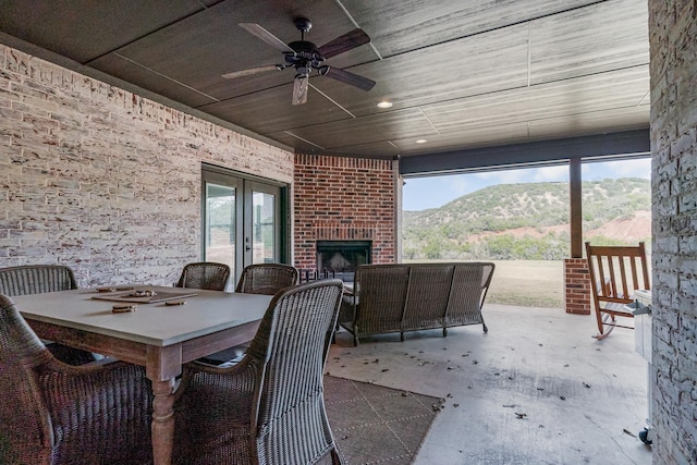 view of patio / terrace with french doors, outdoor dining space, a mountain view, ceiling fan, and an outdoor brick fireplace