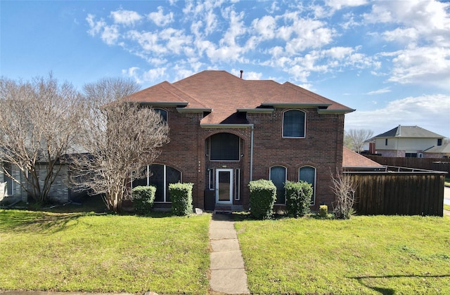 traditional-style house featuring brick siding, a front lawn, and fence