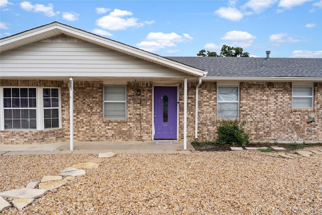 single story home featuring covered porch, brick siding, and a shingled roof