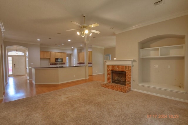 unfurnished living room featuring visible vents, ceiling fan, ornamental molding, built in shelves, and a fireplace