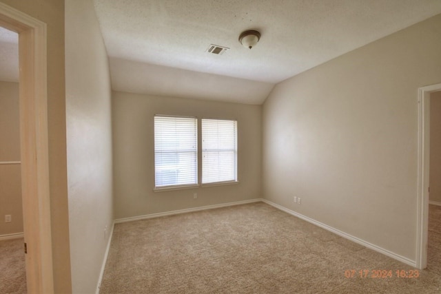 carpeted empty room with baseboards, visible vents, vaulted ceiling, and a textured ceiling