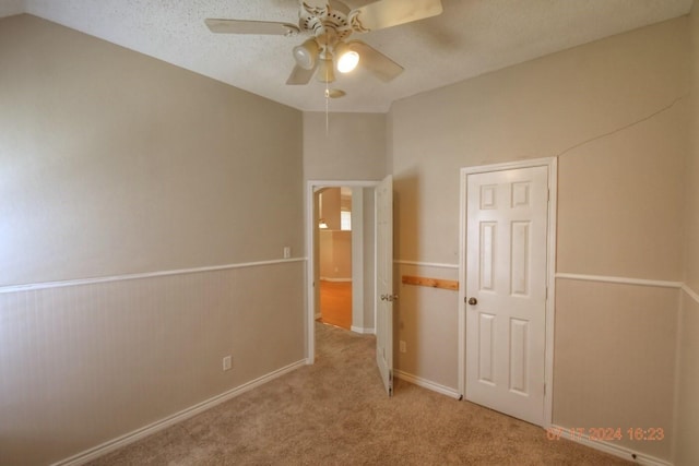 unfurnished bedroom featuring carpet floors, lofted ceiling, wainscoting, ceiling fan, and a textured ceiling