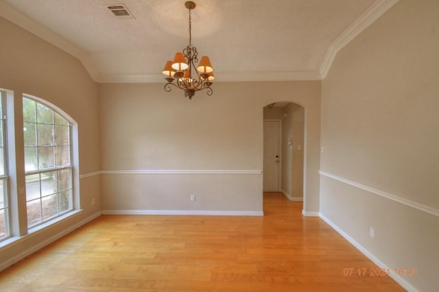 empty room with arched walkways, light wood-style flooring, plenty of natural light, and visible vents