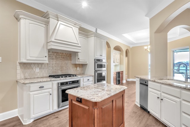 kitchen with light wood finished floors, decorative backsplash, appliances with stainless steel finishes, crown molding, and a sink