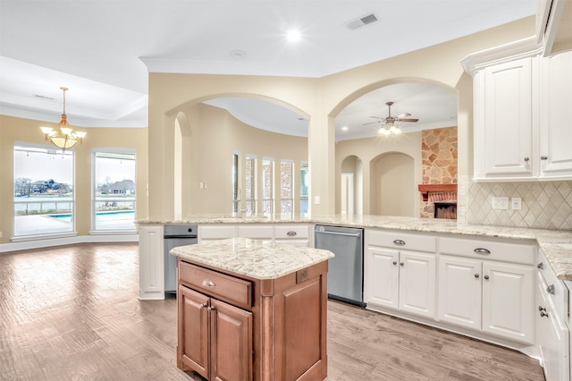 kitchen featuring light stone counters, ceiling fan with notable chandelier, a peninsula, stainless steel dishwasher, and backsplash