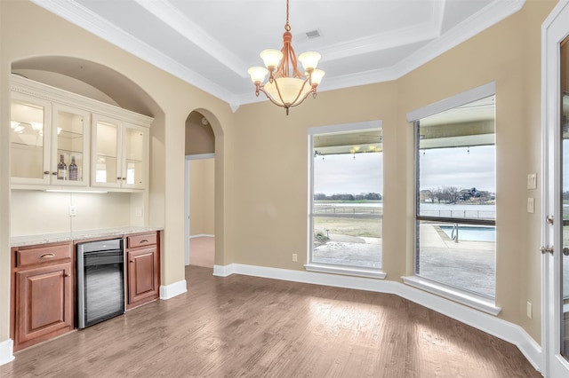 kitchen featuring wine cooler, visible vents, light wood-type flooring, a raised ceiling, and glass insert cabinets