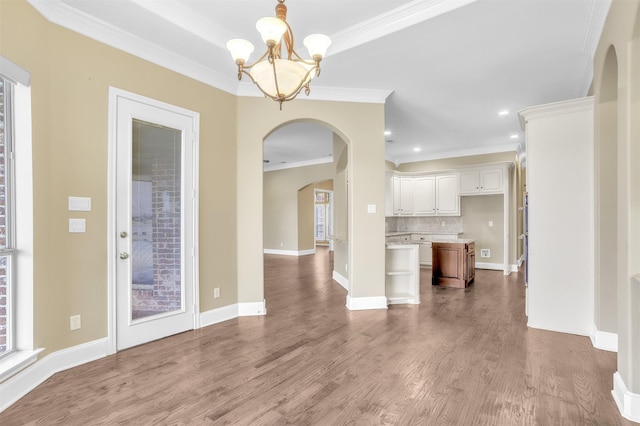 interior space featuring a chandelier, arched walkways, wood finished floors, baseboards, and ornamental molding