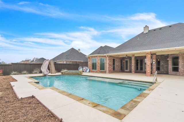view of swimming pool with a water slide, a patio area, a fenced backyard, and an in ground hot tub