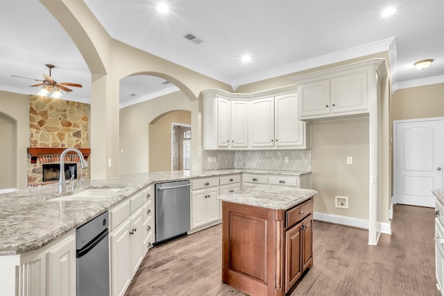 kitchen featuring dishwasher, a stone fireplace, a sink, and ornamental molding