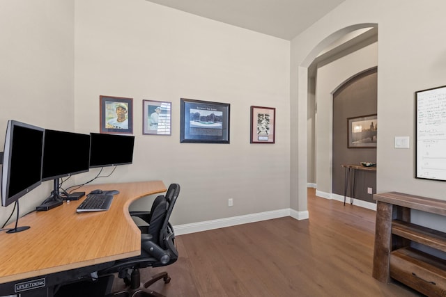 office area featuring baseboards, arched walkways, and wood finished floors