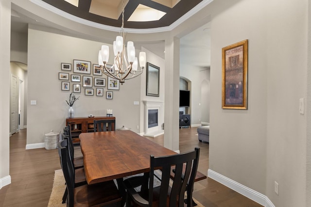 dining area featuring arched walkways, dark wood-style flooring, an inviting chandelier, a glass covered fireplace, and baseboards