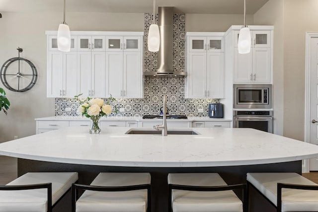 kitchen featuring hanging light fixtures, backsplash, appliances with stainless steel finishes, wall chimney range hood, and a kitchen breakfast bar