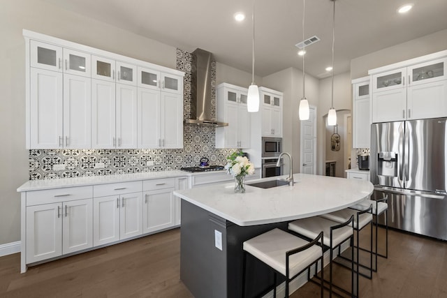 kitchen featuring a center island with sink, visible vents, decorative backsplash, wall chimney exhaust hood, and appliances with stainless steel finishes