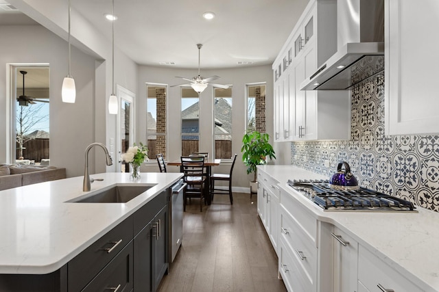 kitchen with white cabinets, decorative backsplash, wall chimney exhaust hood, stainless steel appliances, and a sink