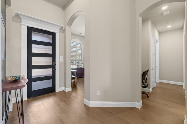 foyer featuring arched walkways, baseboards, and wood finished floors