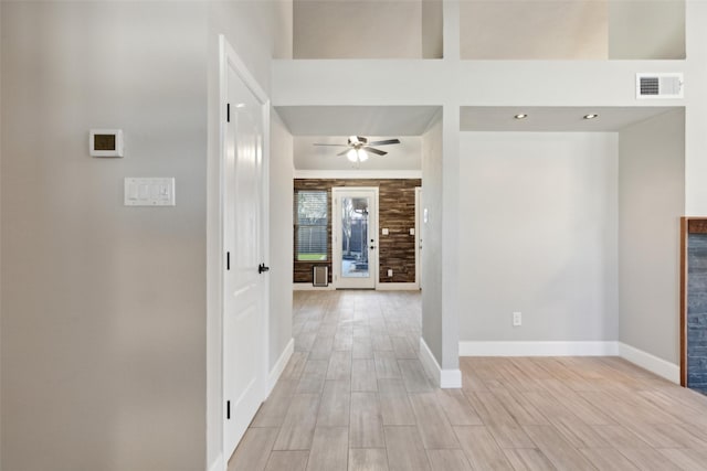 interior space featuring light wood-style floors, a high ceiling, visible vents, and baseboards