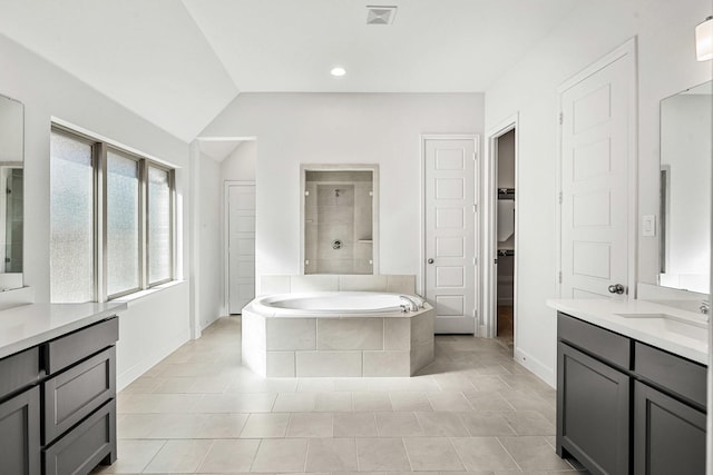 full bath featuring visible vents, a garden tub, two vanities, a sink, and vaulted ceiling