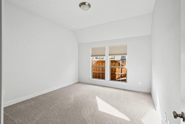 carpeted spare room featuring baseboards and vaulted ceiling