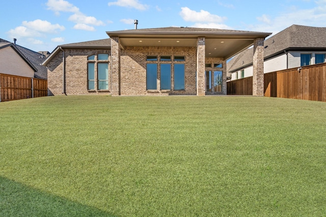 rear view of house with a yard, a fenced backyard, and brick siding