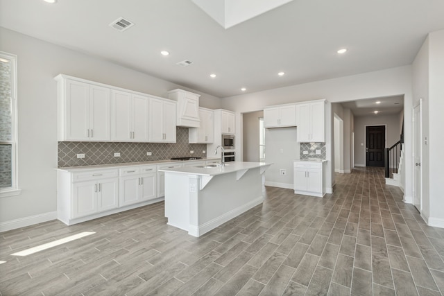 kitchen featuring a center island with sink, light wood finished floors, light countertops, visible vents, and white cabinets