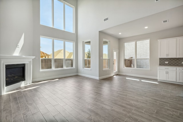 unfurnished living room featuring a glass covered fireplace, wood finished floors, visible vents, and baseboards