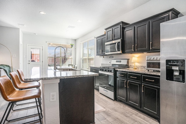 kitchen featuring stainless steel appliances, visible vents, a sink, light wood-type flooring, and dark cabinetry