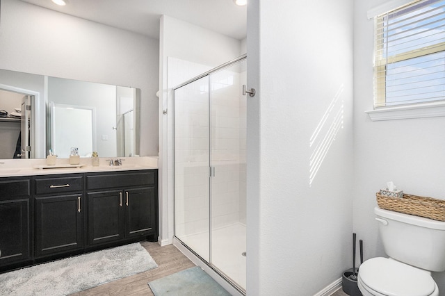 bathroom with double vanity, a stall shower, toilet, and wood finished floors