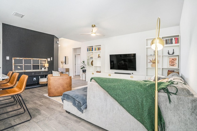 living area featuring built in features, a ceiling fan, visible vents, and wood finished floors