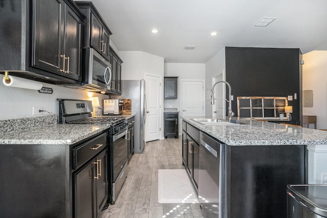 kitchen with a sink, visible vents, appliances with stainless steel finishes, dark cabinetry, and an island with sink