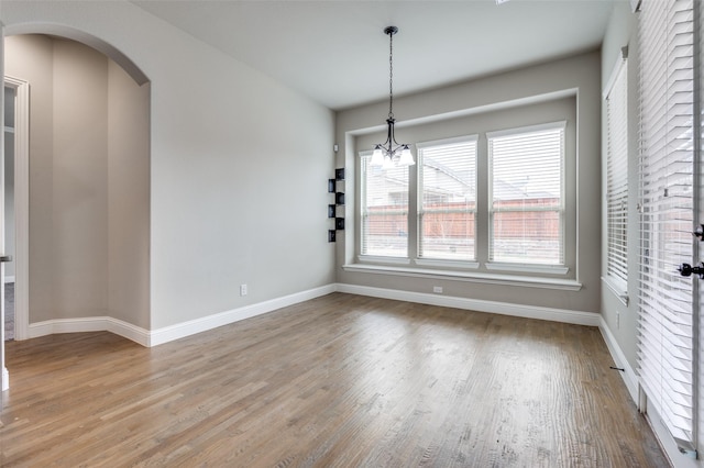 unfurnished dining area with light wood-style flooring, arched walkways, a chandelier, and baseboards