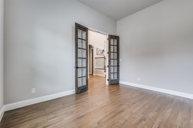 unfurnished room featuring baseboards, arched walkways, wood finished floors, and french doors