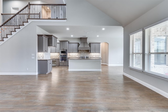 unfurnished living room featuring arched walkways, wood finished floors, high vaulted ceiling, baseboards, and stairs