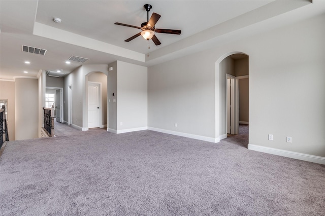 spare room featuring arched walkways, a tray ceiling, carpet, and visible vents