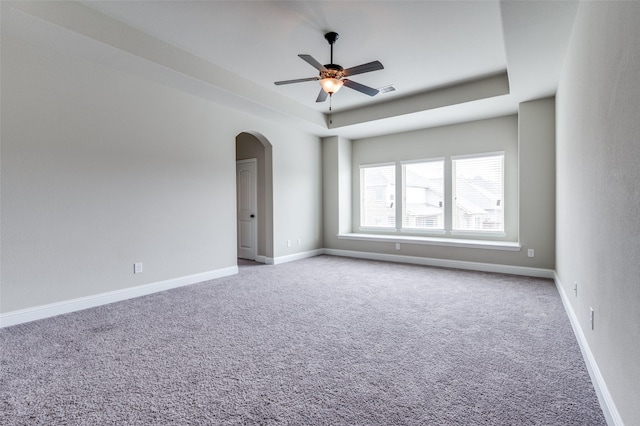 carpeted spare room featuring ceiling fan, baseboards, a tray ceiling, and arched walkways