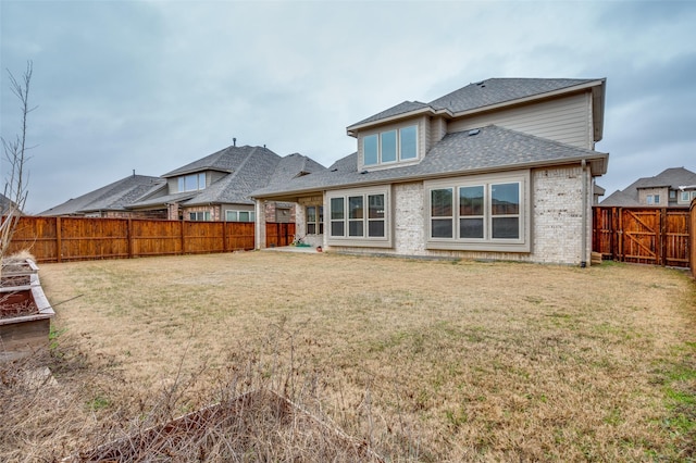 back of property featuring a shingled roof, a fenced backyard, a lawn, and brick siding