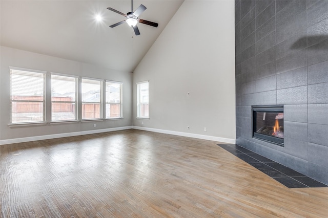 unfurnished living room with high vaulted ceiling, baseboards, a tiled fireplace, and wood finished floors